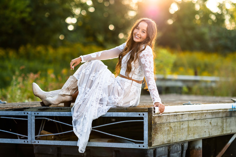 Senior girl in a lace long sleeve crop top and matching maxi skirt with cowboy boots at sunset.