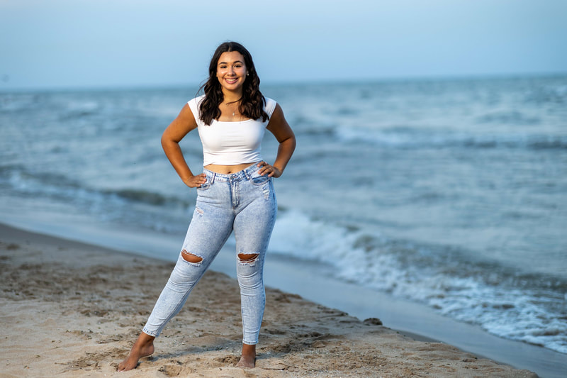 Senior girl, white crop top and jeans at dusk on the beach.