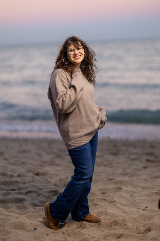 Senior girl with glasses, cozy sweater, and jeans on the beach at sunset
